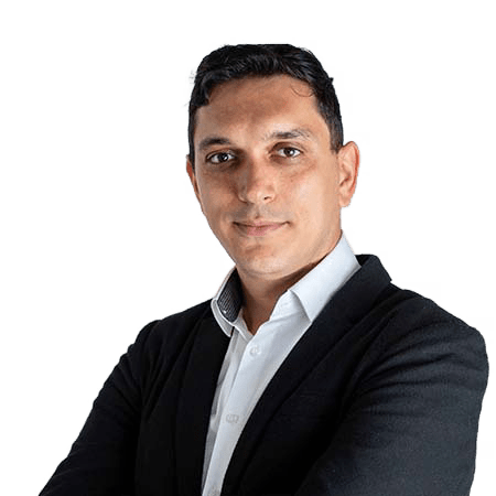Un bărbat care poartă un blazer negru și o cămașă albă stă pe un fundal alb, privind direct la cameră cu brațele încrucișate, emanând încredere asemănătoare unui expert SEO care analizează tendințele de căutare.