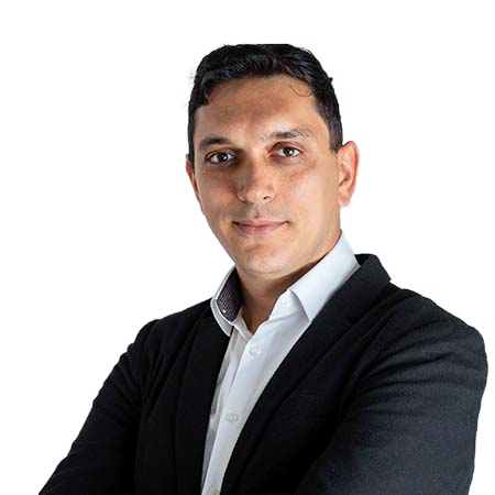 Un bărbat care poartă un blazer negru și o cămașă albă stă pe un fundal alb, privind direct la cameră cu brațele încrucișate, emanând încredere asemănătoare unui expert SEO care analizează tendințele de căutare.