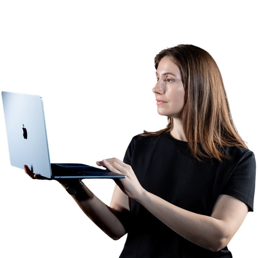 O femeie în cămașă neagră ține și folosește un laptop deschis, probabil lucrând la sarcini SEO, în timp ce privește spre dreapta, pe un fundal alb simplu.