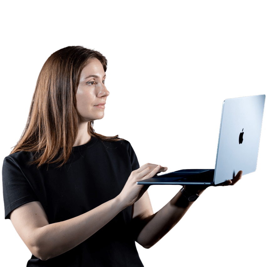 O femeie în cămașă neagră folosește un laptop Apple argintiu, probabil căutând Servicii SEO București, în timp ce se uită la stânga ei pe un fundal alb.