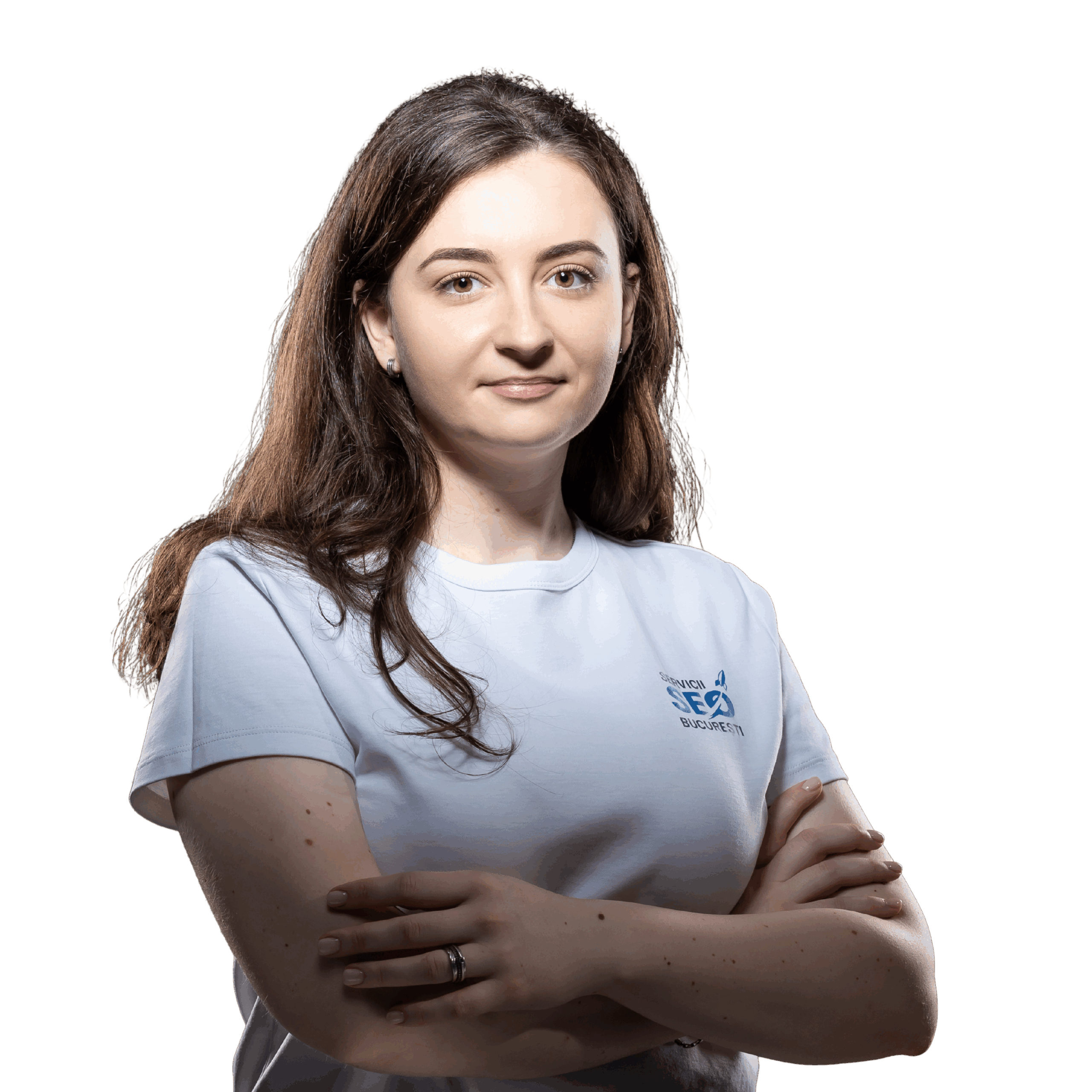 O femeie cu păr șaten lung, îmbrăcată cu un tricou alb, stă cu brațele încrucișate, privind cu încredere la cameră, pe un fundal alb simplu, surprinzând esența unui profesionist SEO modern.